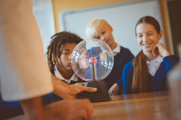 Group of student listening to female teacher showing plasma ball during physics lesson.