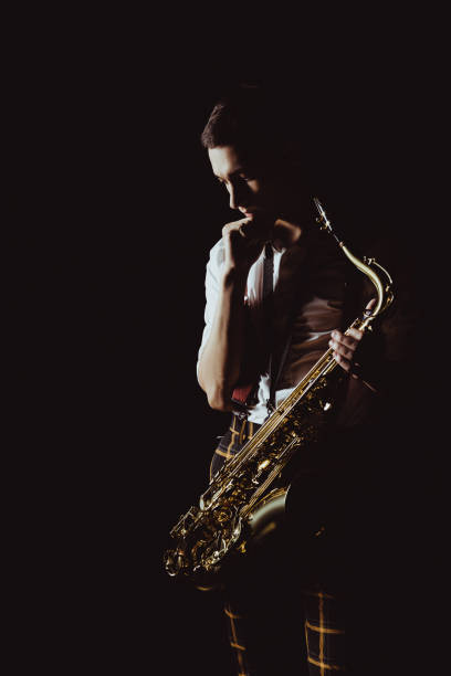 istock pensive young musician holding saxophone isolated on black 1003417258