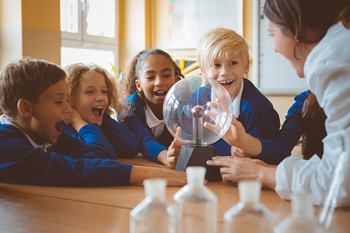 Group of school kids listening to female teacher showing plasma ball during physics lesson.