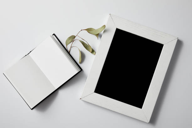 istock top view of opened notebook with green leaves and blank frame on white surface for mockup 1003422808