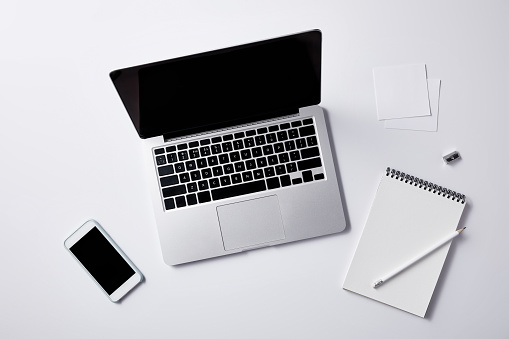 top view of workplace with laptop and smartphone on white tabletop for mockup