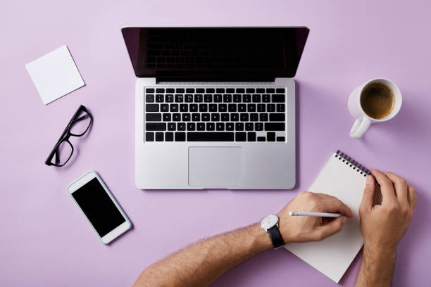 istock cropped shot of man writing in notebook at workplace on pink surface for mockup 1003422938
