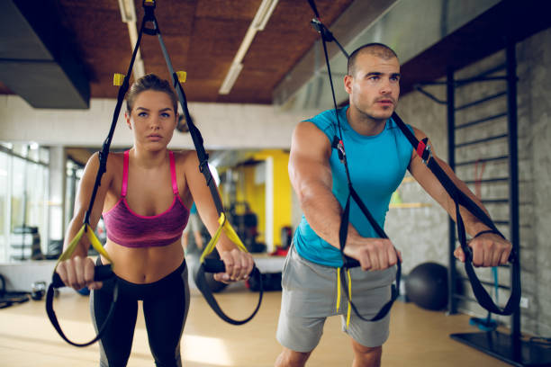 istock Couple doing arm exercises with suspension straps at gym 1003427660