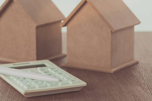 istock small wooden houses and calculator with pen on table, saving concept 1003431476