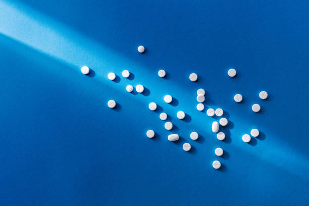 istock elevated view of white tablets on blue background with sunlight 1003454884