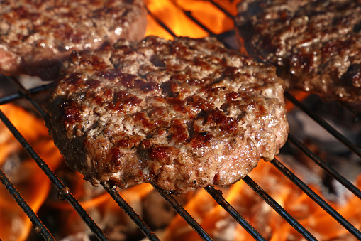 Close-up of beef burger patties getting roasted together with burger bread on a charcoal barbecue grill.