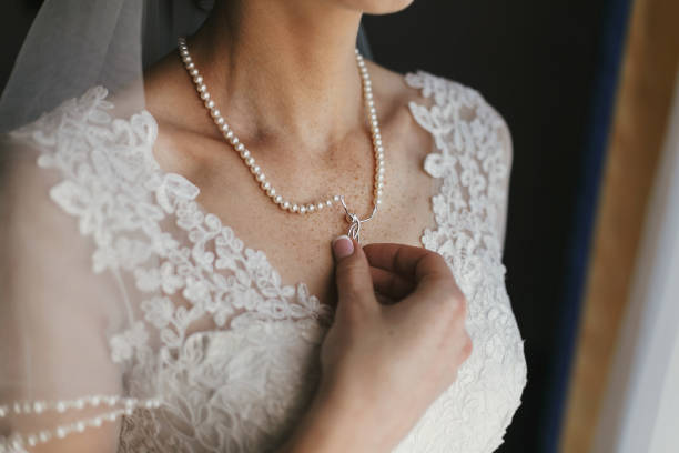 belle mariée tenant cher collier en argent avec perles sur le cou. femme en robe blanche avec ornements floraux de dentelle, préparatifs mariée matin. bijoux élégant. photo boudoir - veil bride lace married photos et images de collection