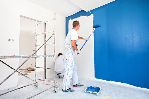 House painters beginning to paint a large blue wall. Professional house painters in bright room.