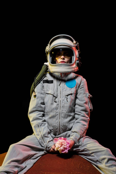 female astronaut in spacesuit and helmet sitting on planet with flower in cosmos - spacewoman imagens e fotografias de stock