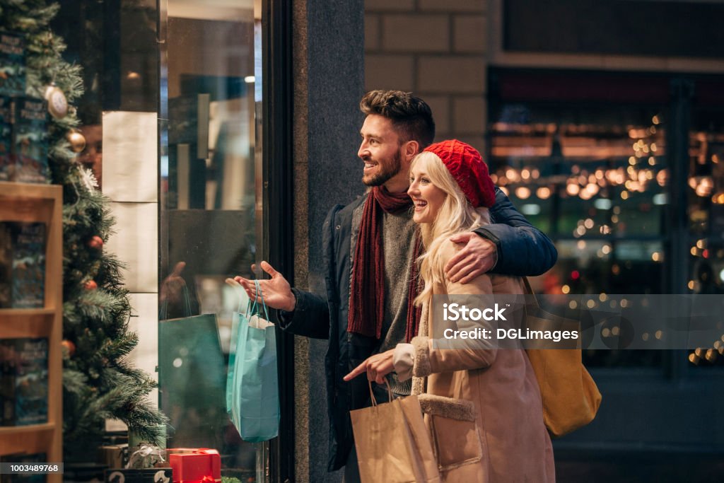 Couple Doing Some Window Shopping Side view of a couple doing some window shopping at christmas. The mid adult male has his arm around the mid adult female and they are talking about wats in the window. Shopping Stock Photo