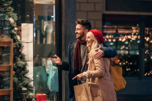 Couple Doing Some Window Shopping Side view of a couple doing some window shopping at christmas. The mid adult male has his arm around the mid adult female and they are talking about wats in the window. window shopping stock pictures, royalty-free photos & images
