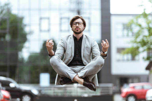 attractive young businessman floating in air in lotus pose and meditating at parking - lotus automobiles imagens e fotografias de stock