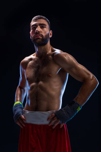 istock Handsome athletic guy in a red shorts on a black background. The boxer is fetching his breath after practicing hooks and blows 1003490708