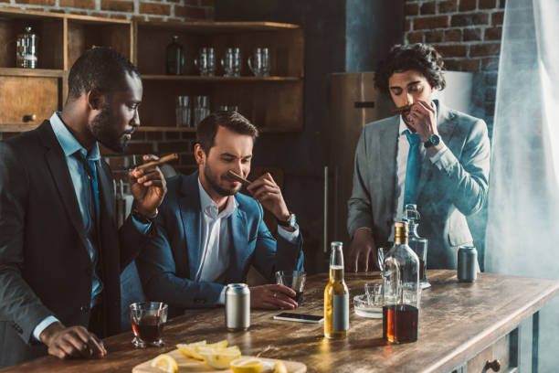 handsome young multiethnic men in suits holding cigars while partying together handsome young multiethnic men in suits holding cigars while partying together cigar photos stock pictures, royalty-free photos & images