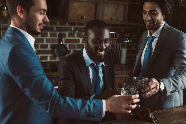 smiling young multiethnic male friends in suits clinking glasses of whiskey smiling young multiethnic male friends in suits clinking glasses of whiskey stag night stock pictures, royalty-free photos & images