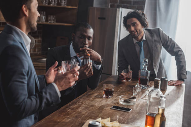 istock cropped shot of smiling multiethnic businessmen talking while smoking cigars and drinking whiskey 1003529574
