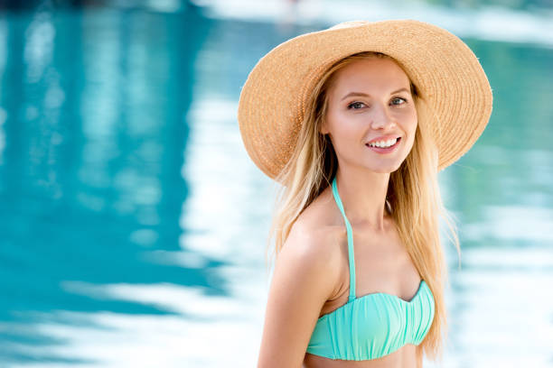 istock attractive young woman in straw hat and bikini looking at camera at poolside 1003534004