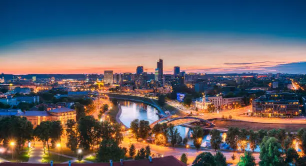 Photo of Vilnius, Lithuania. Modern Office Buildings Skyscrapers In Business District New City Center Shnipishkes In Night Illuminations. Panoramic View Cityscape At Sunset.