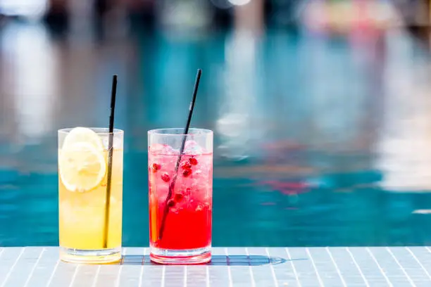 close-up shot of glasses of delicious red and orange cocktails on poolside