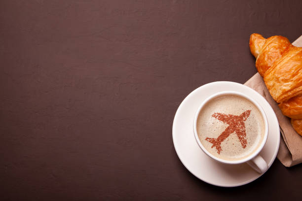 Cup of coffee with an airplane on the foam. Morning coffee with croissant in flight stock photo