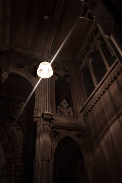 istock Electric light bulb hangs from a beamed ceiling in a gloomy monastery 1003580730