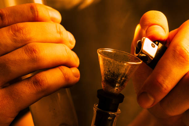 istock A man smokes cannabis weed, Bong lighter in his hands. Smoke on Yellow toning 1003584580