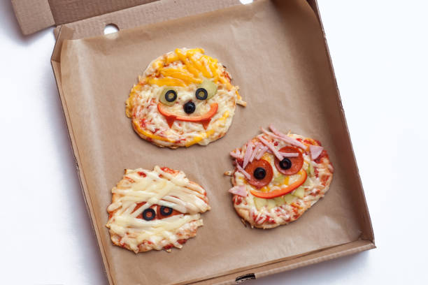 istock Halloween pizza with monsters, above scene with decor on a craft paper box background, idea for home party food, easy, healthy and delicious fun food party treats for kids 1003589470