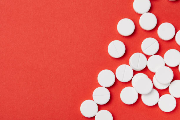 istock A few white round pills on the red paper background. 1003594226