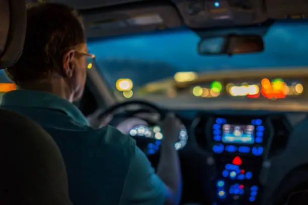 Passenger view of a man driving an SUV on a freeway in Utah, USA at night, with the freeway lights in the distance and the car's dashboard lights in the foreground.   Shallow depth of field.