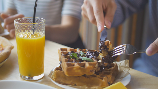 Male hands cuts a yummy belgian waffles with a knife and fork in restaurant, close up