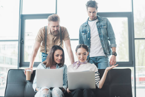 istock Successful business people working on laptops while sitting on sofa in modern light office 1003598988