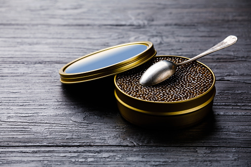 Black caviar in can and spoon on black wooden background copy space