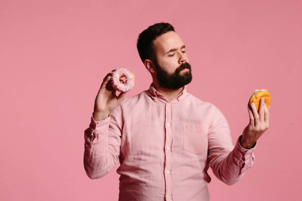 istock Man holding and looking at donut and thinking about eating it 1003611270