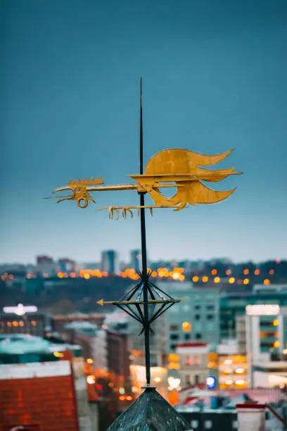 Photo of Tallinn, Estonia, Europe. Cock-rope Weather Vane On Roof Of Old Medieval House In Winter Evening In Night Illuminations Lights