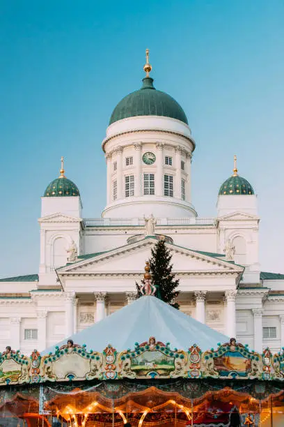 Photo of Helsinki, Finland. Xmas Market On Senate Square With Holiday Carousel And Famous Landmark Is Lutheran Cathedral And Monument To Russian Emperor Alexander II At Winter Evening