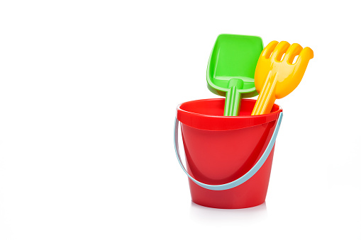 Front view of a sand bucket, pail and shovel taken on reflective white background. The objects are grouped at the right of an horizontal frame leaving useful copy space for text and/or logo at the center-left. Predominant colors are red and white, but also are present green and yellow. High key DSRL studio photo taken with Canon EOS 5D Mk II and Canon EF 100mm f/2.8L Macro IS USM.