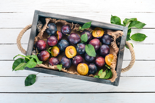 Plums with leaves in a wooden box. On a white wooden background. Top view. Free space for your text.