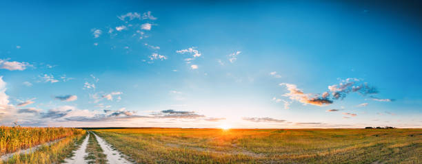 Sunset, Sunrise Over Rural Meadow Field And Country Road. Countryside Landscape With Path Way Under Scenic Summer Dramatic Sky In Sunset Dawn Sunrise. Sun Over Skyline Or Horizon stock photo