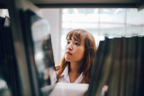 Young Asian student searching through the shelves of the library, searching for books for her studies.