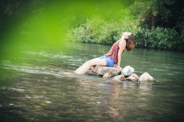 istock Girl sitting on a stone in the river 1003676310