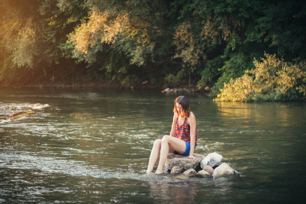 istock Girl sitting on a stone in the river 1003678972