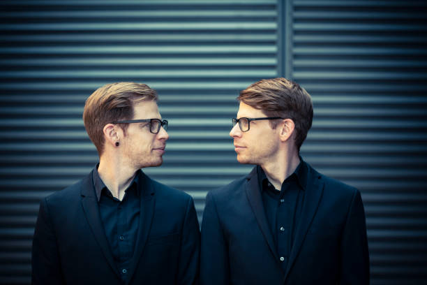 twin brothers face to face portrait twin brothers with black suits and glasses standing and looking into each other eyes. two men same clothes stock pictures, royalty-free photos & images