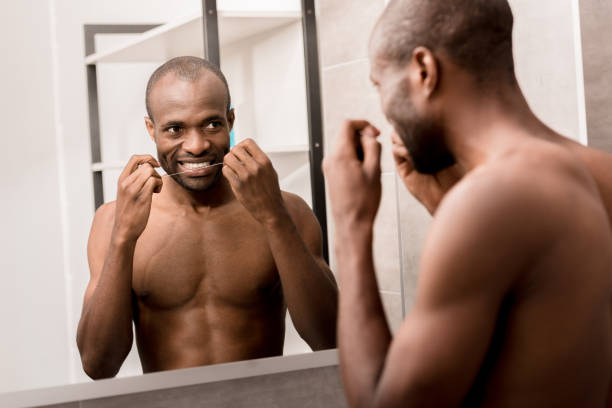 istock happy young man cleaning teeth with dental floss while looking at mirror in bathroom 1003735602
