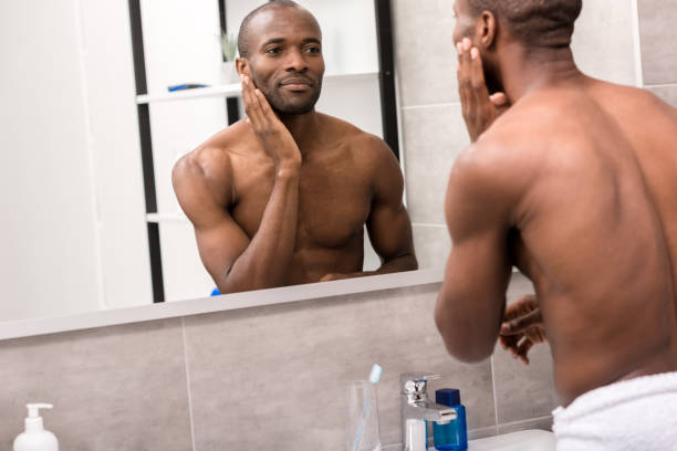 istock handsome young man applying facial lotion after shaving while looking at mirror in bathroom 1003735672