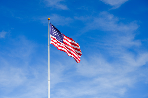 A large USA flag of stars and stripes flying high in strong wind on a sunny day in springtime.