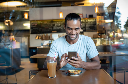 Portrait of a happy young man texting on his cell phone at a cafe and looking happy - lifestyle concepts