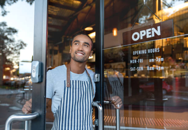 happy waiter opening on the doors at a cafe - minority imagens e fotografias de stock