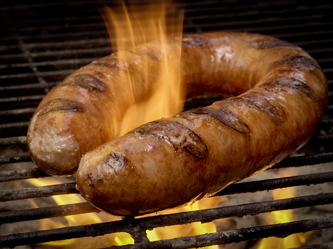 Polish sausage with juices dripping into the hot flames of an old fashioned charcoal barbecue grill