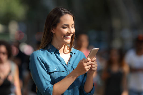 istock Smiley girl using a smart phone walking in the street 1003790108