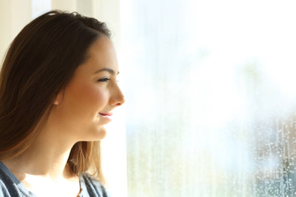 istock Happy girl looking through a window after the rain 1003790470